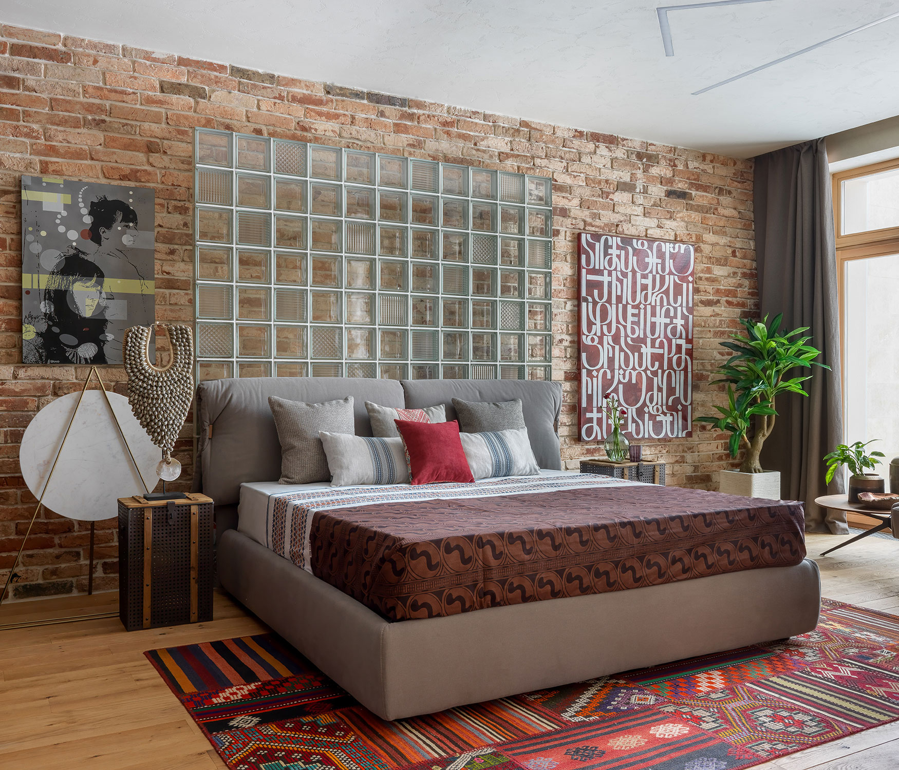 A gray bed in a room with exposed brick and an ornate red rug