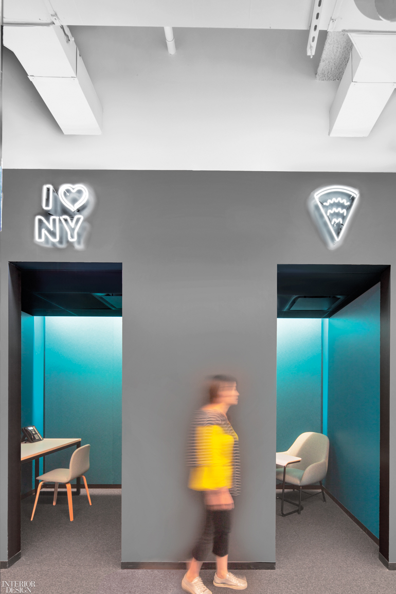 A woman walks by telephone booth-inspired work areas with neo signs above