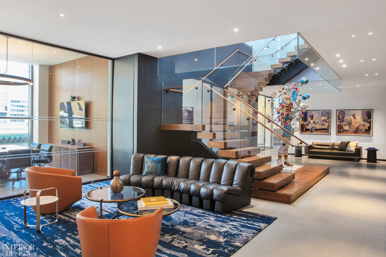 inviting lobby space with brown couch, orange armchairs and view of office space and staircase