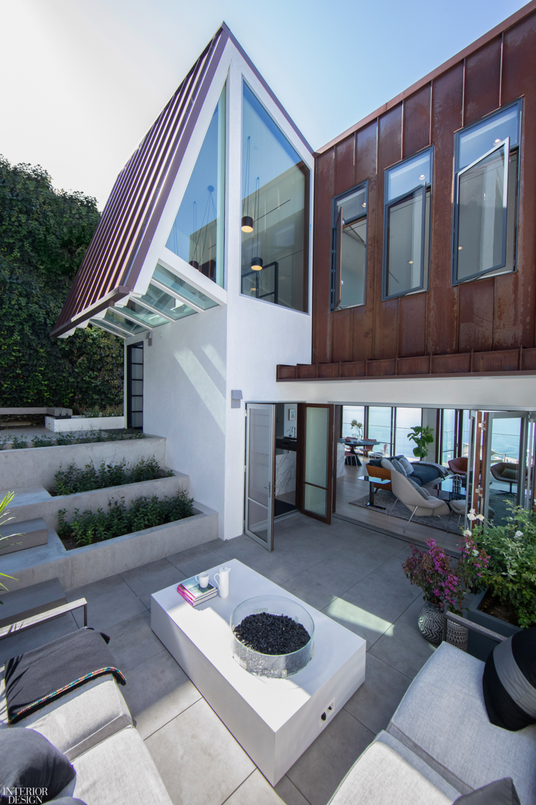 The facade of a modern geometric home with a large patio with white furniture 