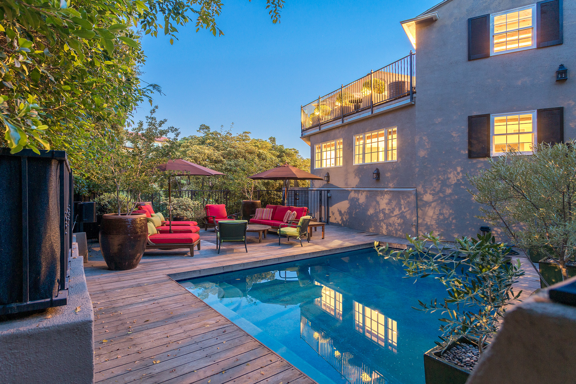 A home deck with a pool and red patio furniture at dusk