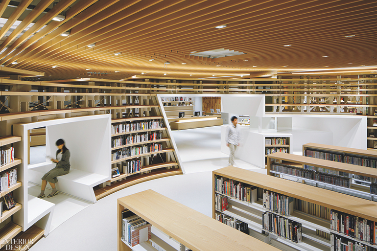 visitors walk throughout a Japanese library with curving bookcases and cutouts between bookcases for seats