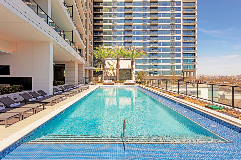 An outdoor lap pool with blue and teal tiles surrounded by palm trees