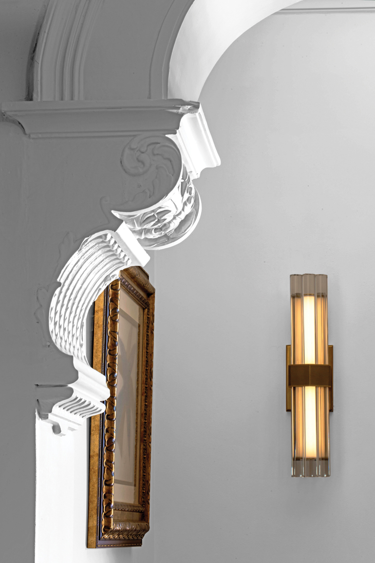 In the lobby, an original carved pilaster meets Lauren Rottet’s LED Fascio sconce in antique brass