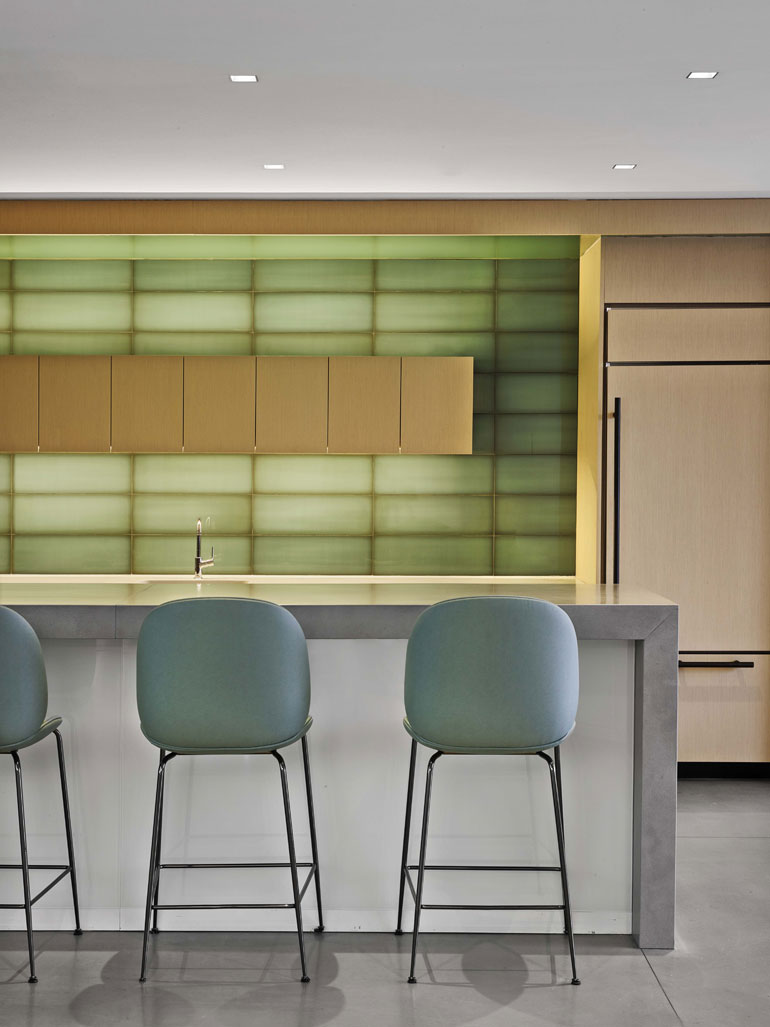 a muted green wall behind a gray kitchen island with blue-green backed bar stools