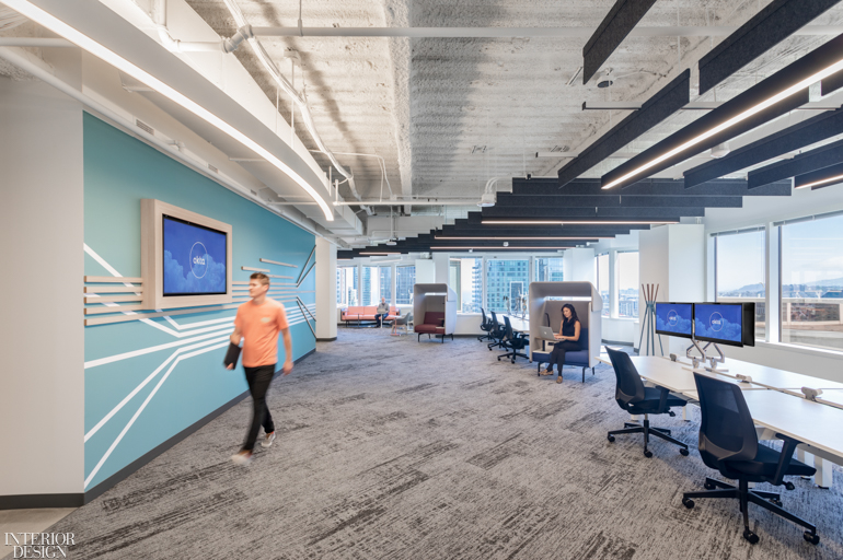 A man in a peach t-shirt walks through workstations at the Okta office