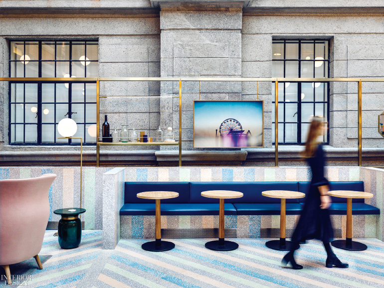 a woman walks past an office kitchen with blue booth seats and flooring with diagonal blue, yellow, and green lines